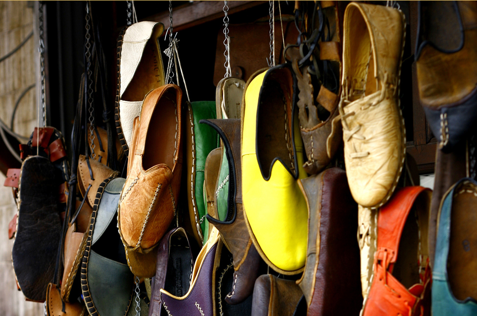 这张照片显示了许多不同颜色的不同鞋子。 鞋子好像是用绳子挂在墙上的。