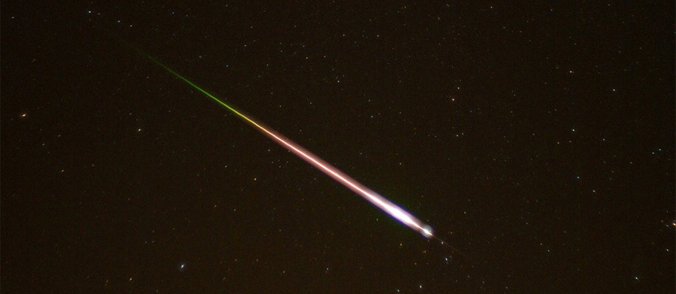 Esta é uma foto tirada do céu noturno. Um meteoro e sua cauda são mostrados entrando na atmosfera terrestre.