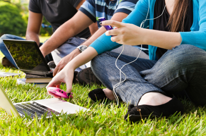 Students sitting outdoors with laptop computers, cell phones, and mp3 players